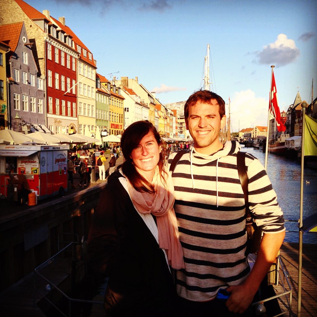 man and woman smiling in front of colorful buildings and river
