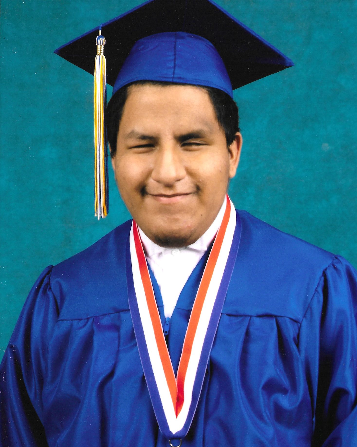 boy wearing blue graduation cap and gown and gold medal