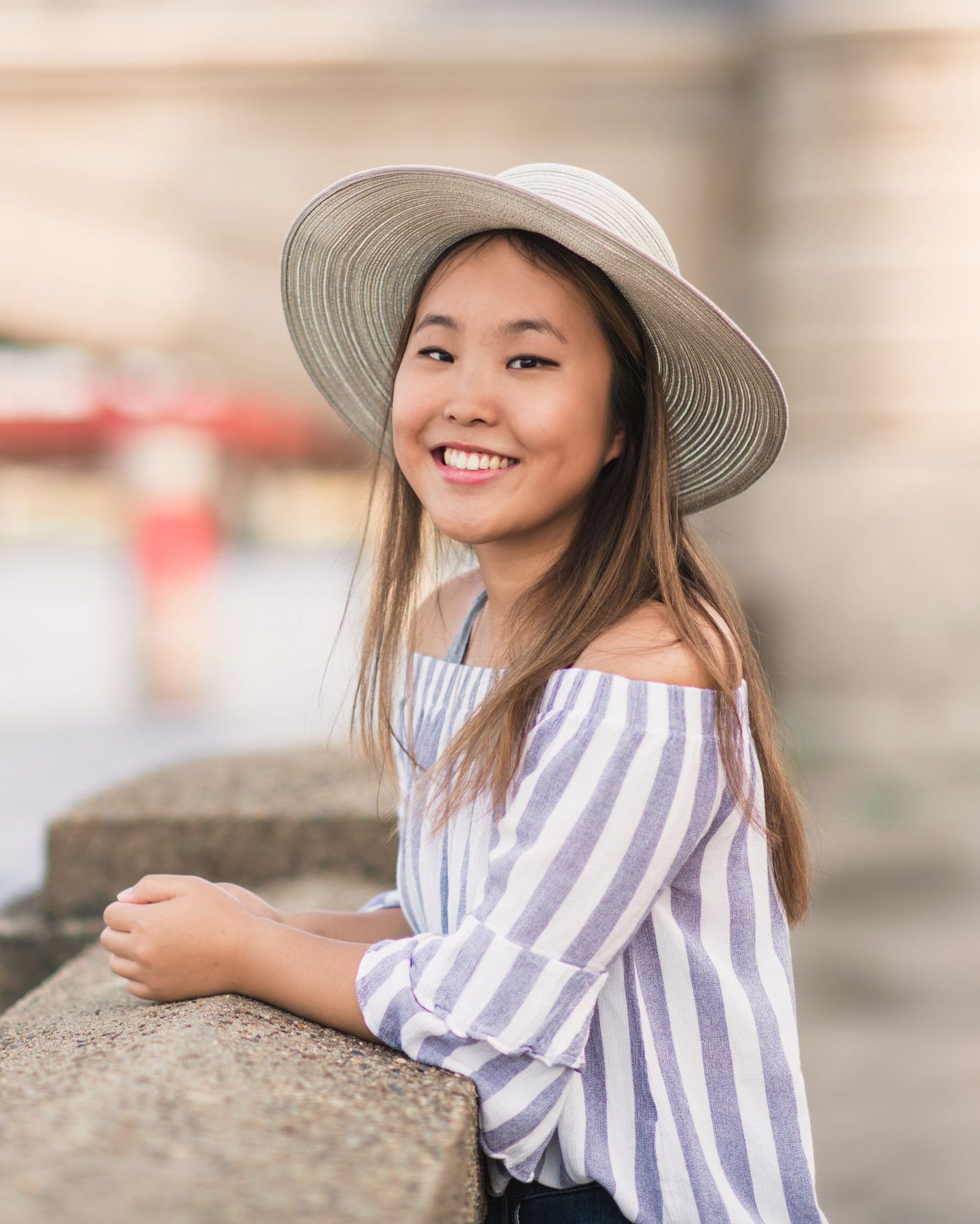 girl leaning on fence wearing striped shirt and woven sunhat