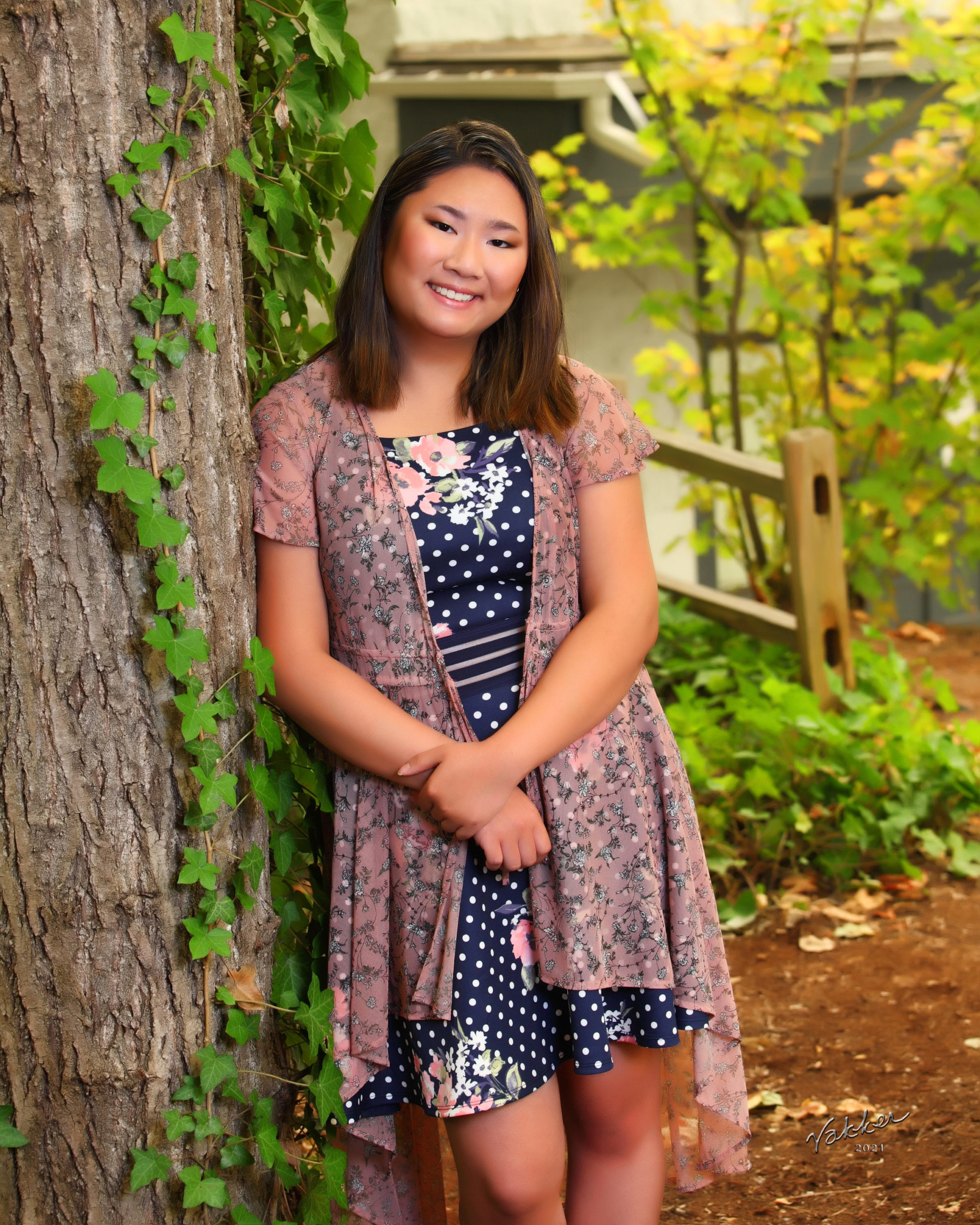 smiling girl wearing flowered dress leaning on tree