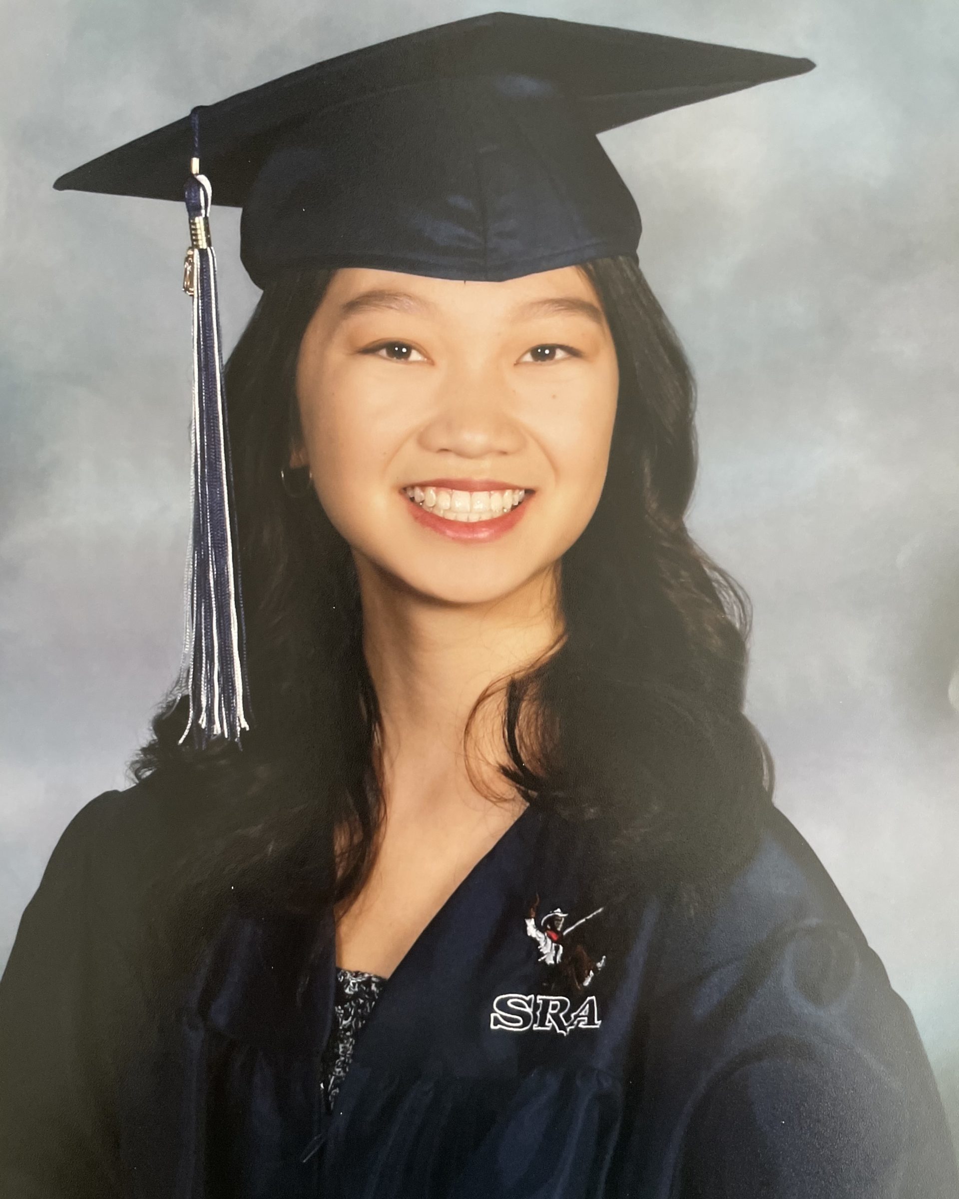 smiling girl wearing navy graduation gown and cap