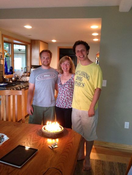 two men and one woman standing behind a cake with lit candles