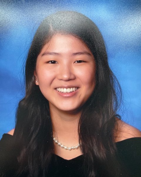 school photo of smiling girl in black off the shoulder top in front of blue background