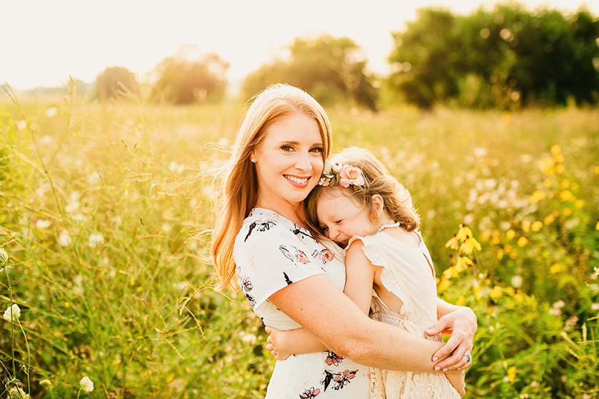 sunlit photo of woman and daughter embracing in grassy field