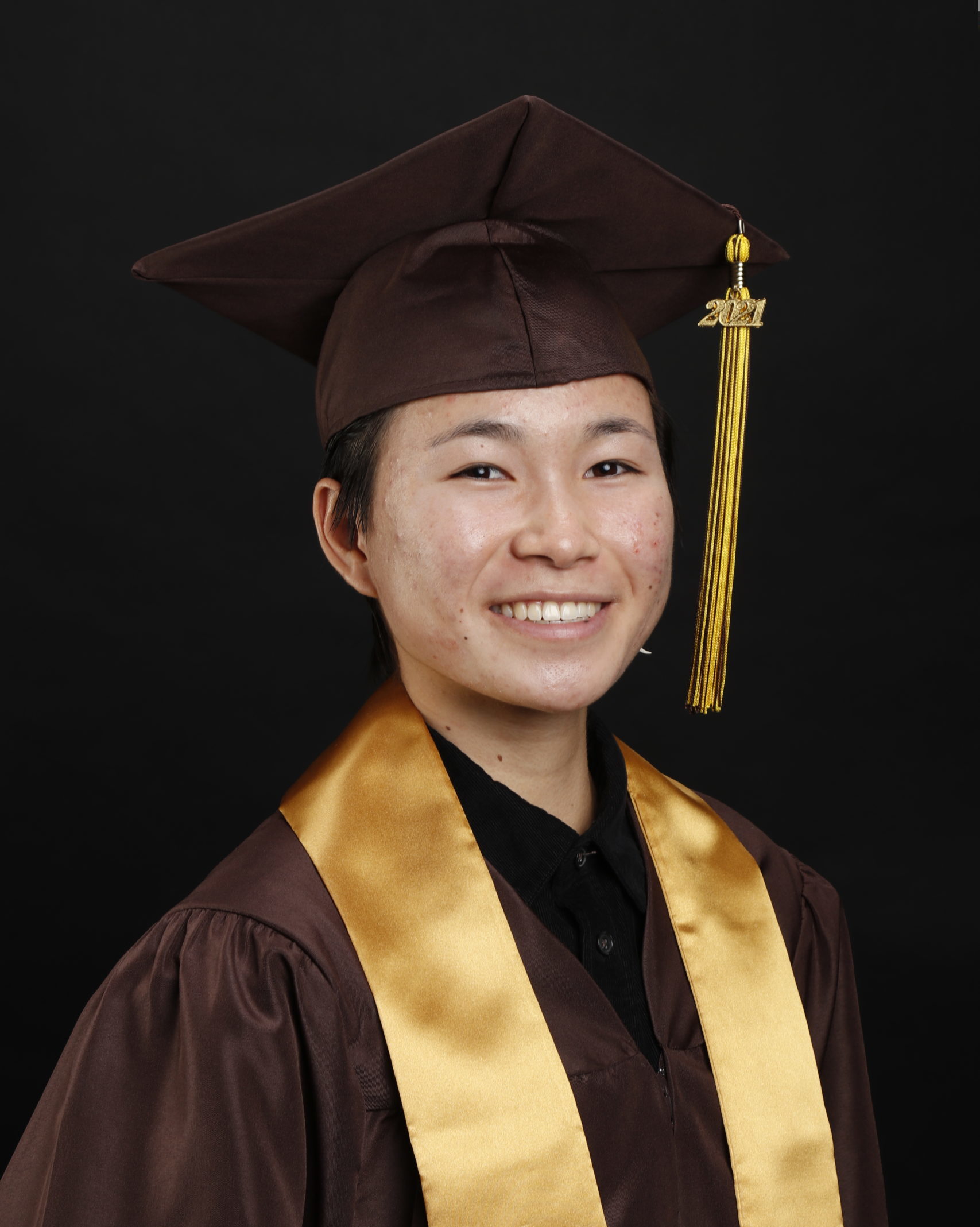 smiling girl in brown graduation cap and gown and yellow sash