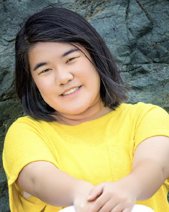 smiling girl sitting on boulder in yellow shirt