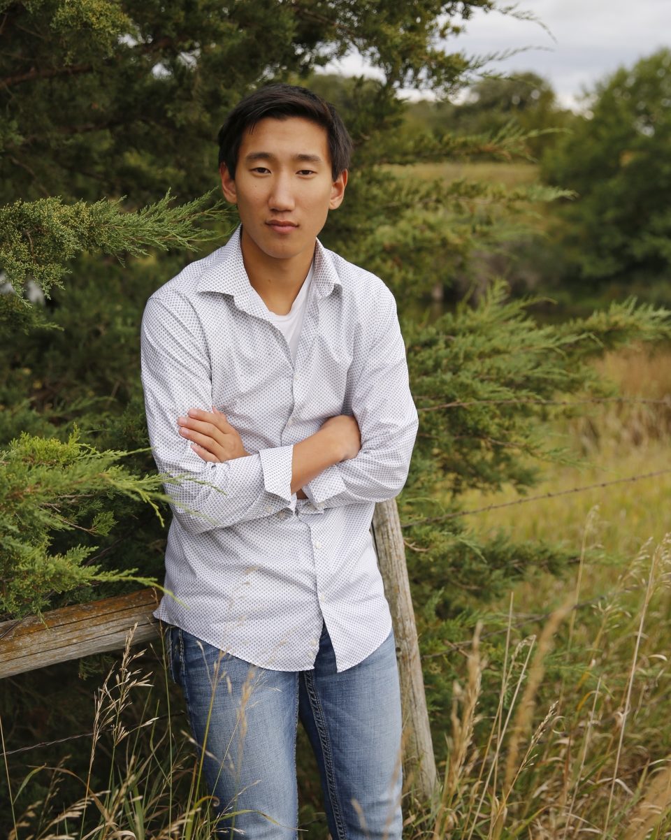 man with arms folded leaning on fence in grassy field