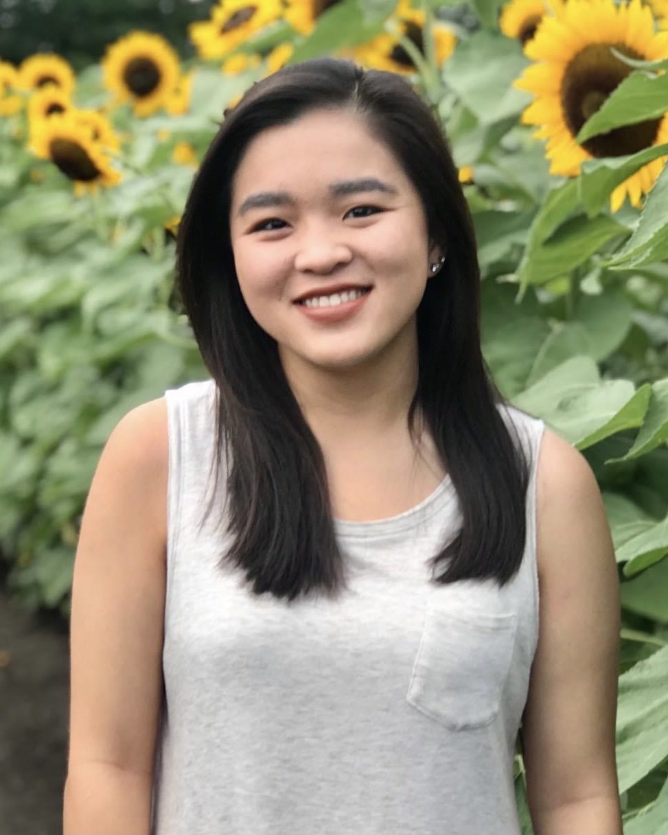 smiling girl in white tank top in front of tall sunflowers