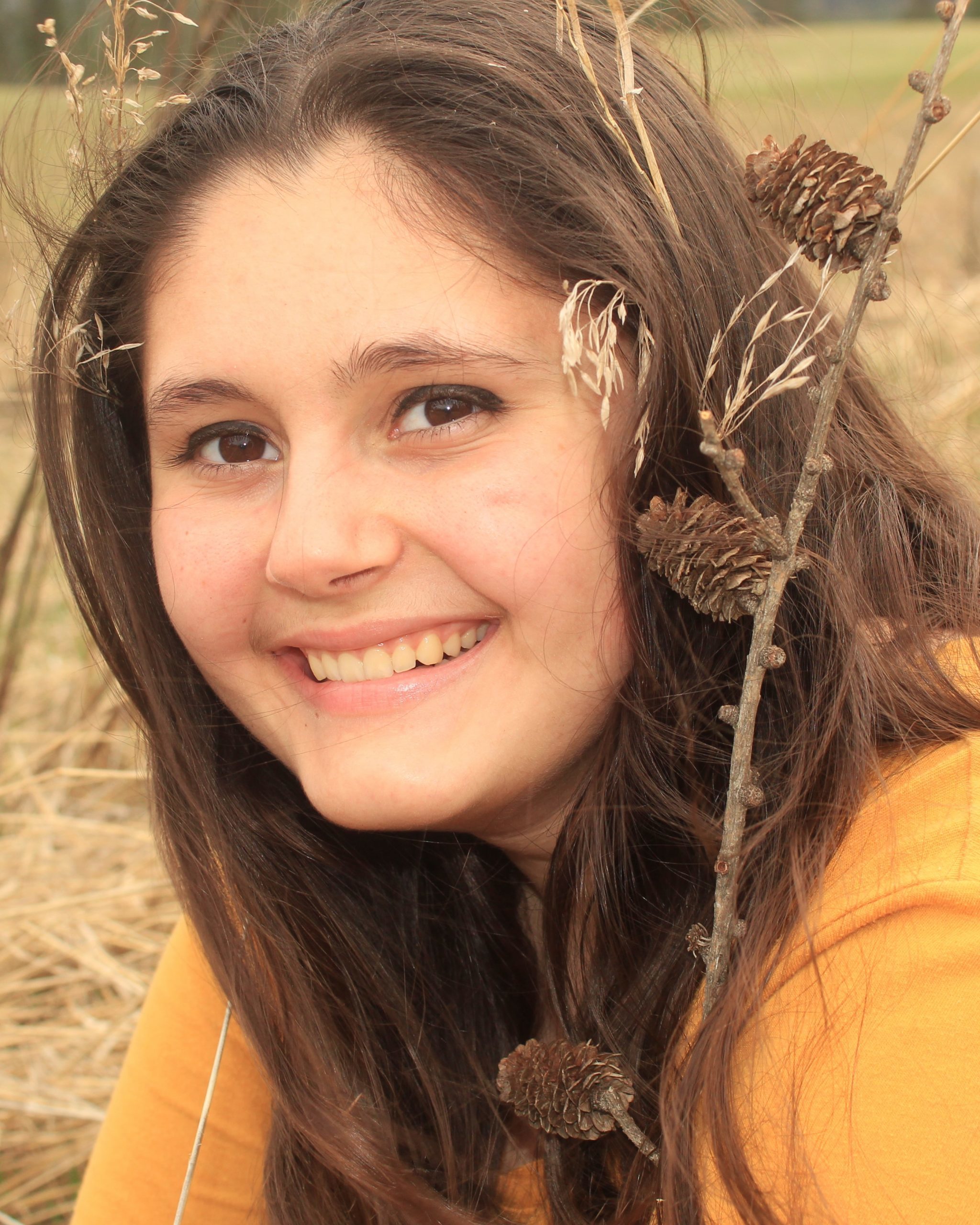 smiling girl with brown hair laying in wheat field