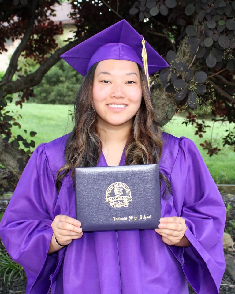smiling girl wearing purple graduation cap and gown holding diploma