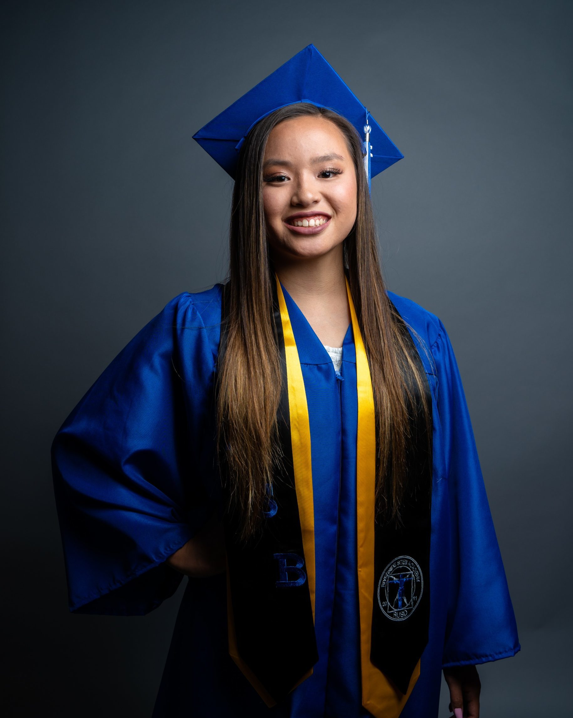 smiling girl standing with one hand on hips wearing blue graduation cap and gown