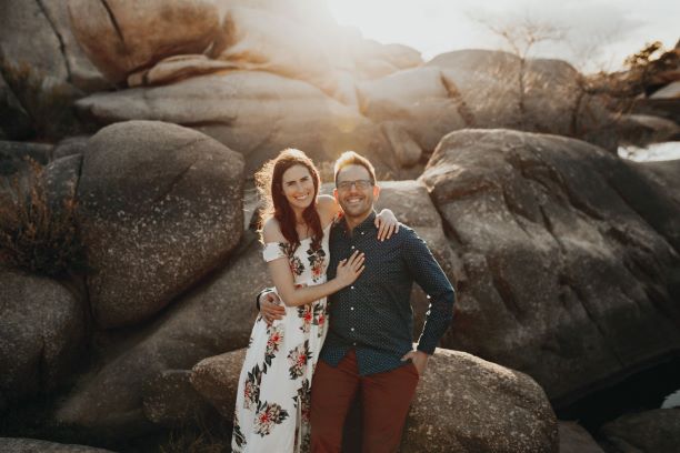 smiling woman with her arms around a man in front of grey boulders