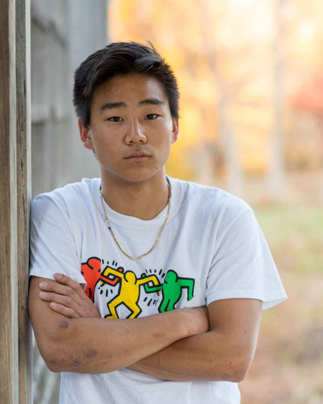 man wearing keith haring graphic shirt with arms across leaning against a wall