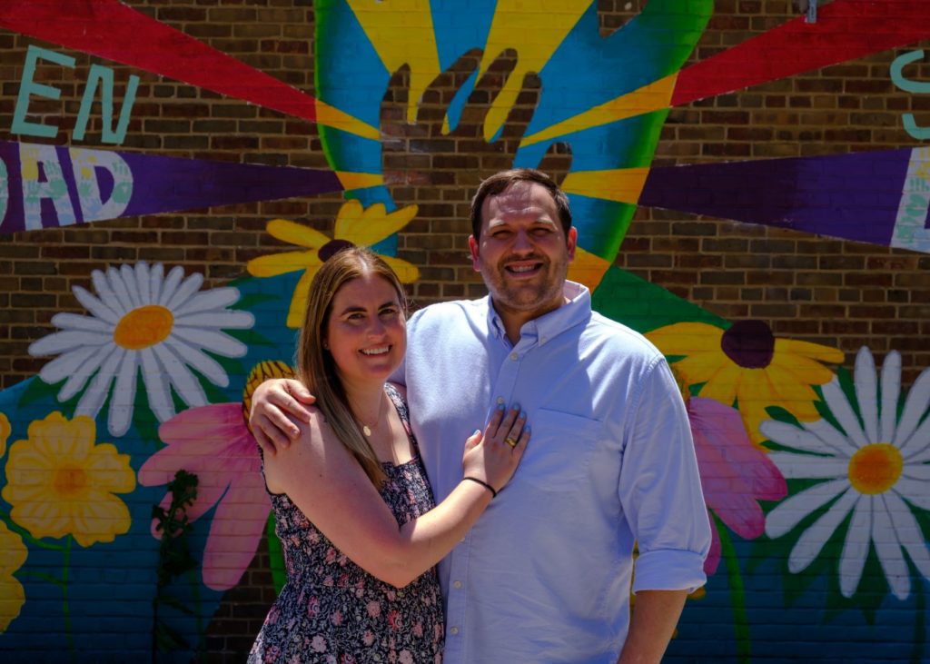 smiling man and woman in front of brick wall with flowered street art