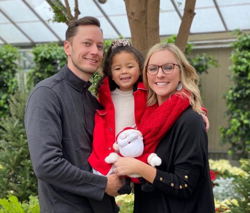 man and woman holding little girl in red coat and santa doll