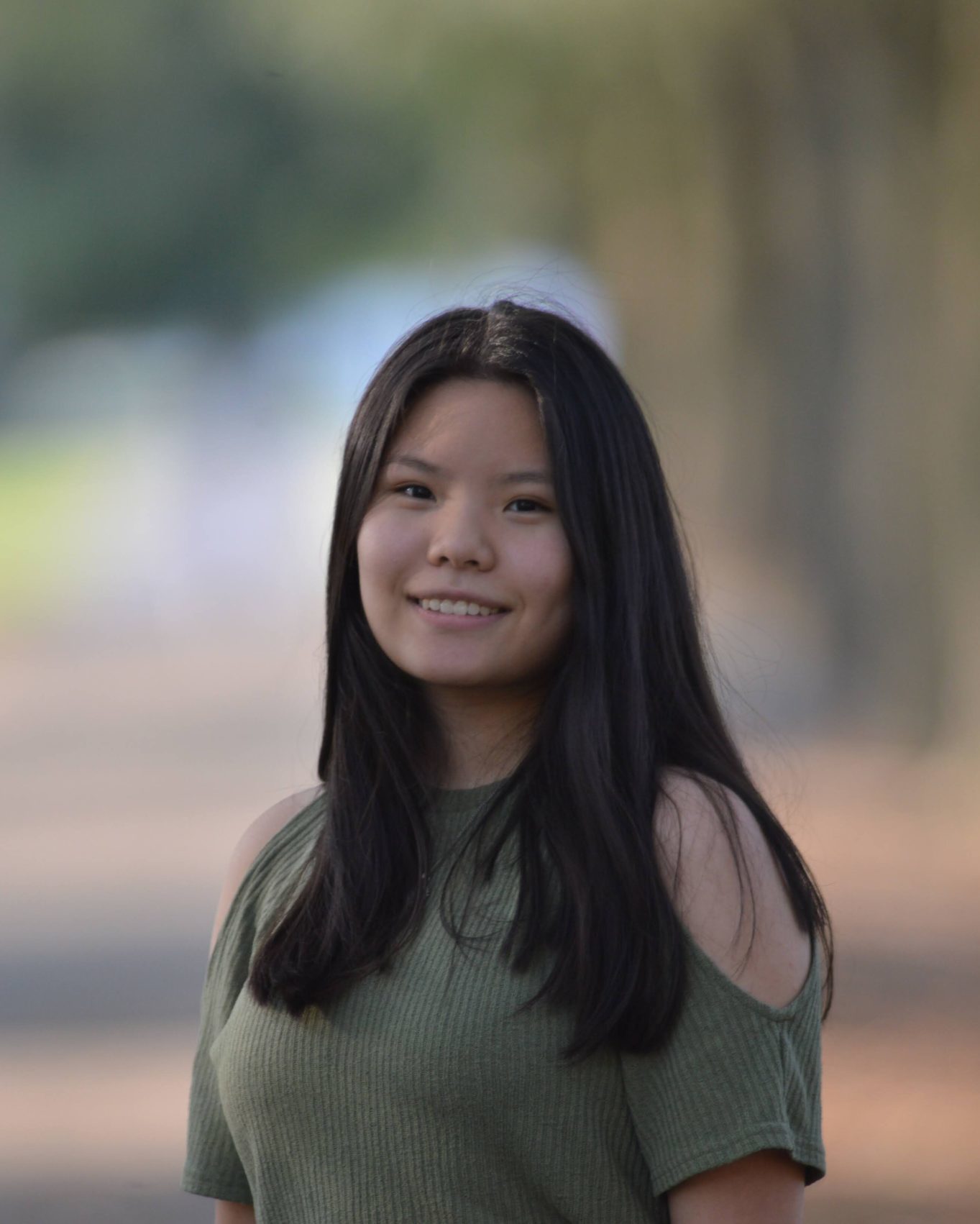 smiling girl wearing green shirt in center of frame with blurred background