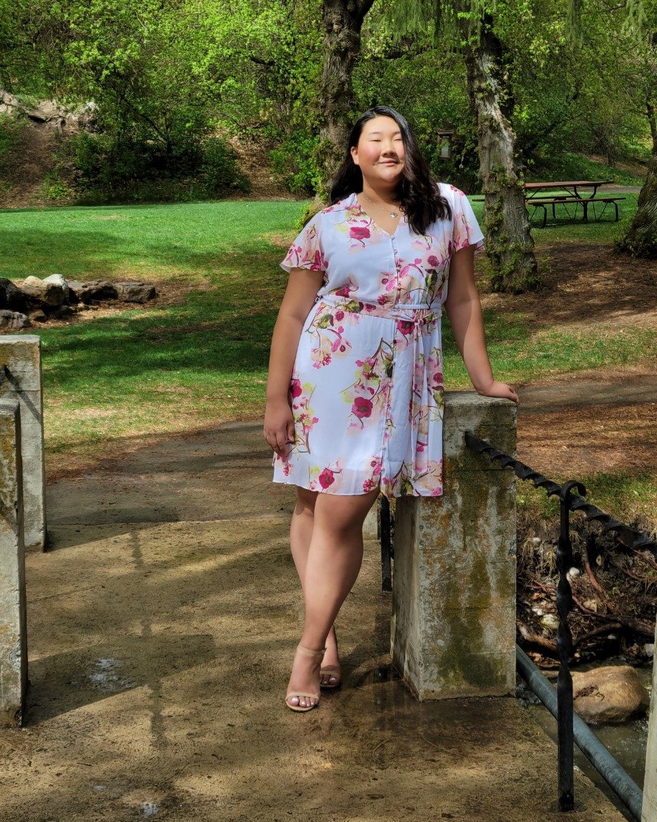 girl leaning against fence wearing floral dress