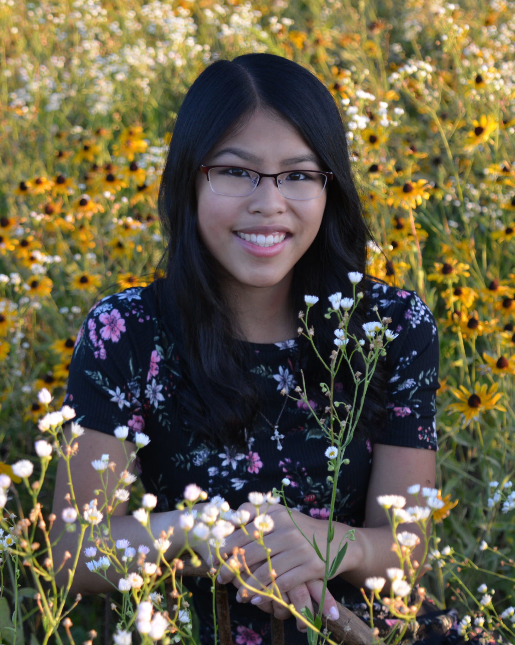 smiling girl sitting in field of flowers wearing floral dress and glasses
