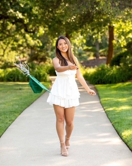 smiling girl wearing white dress walking down path and tossing green graduation cap