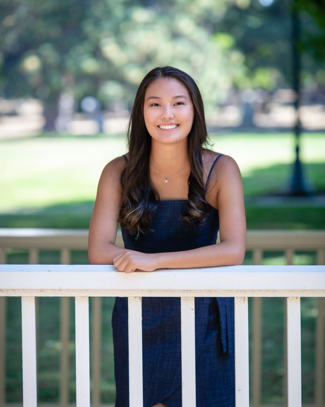 smiling girl in navy blue dress leaning on white fence