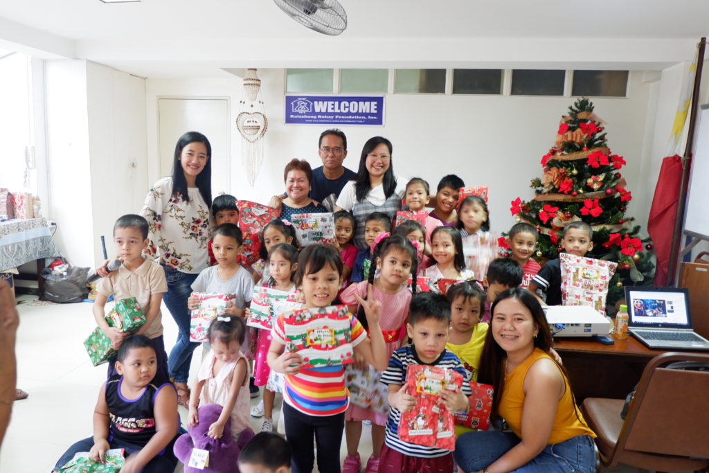 group of foster children and caregivers in front of a Christmas tree holding presents