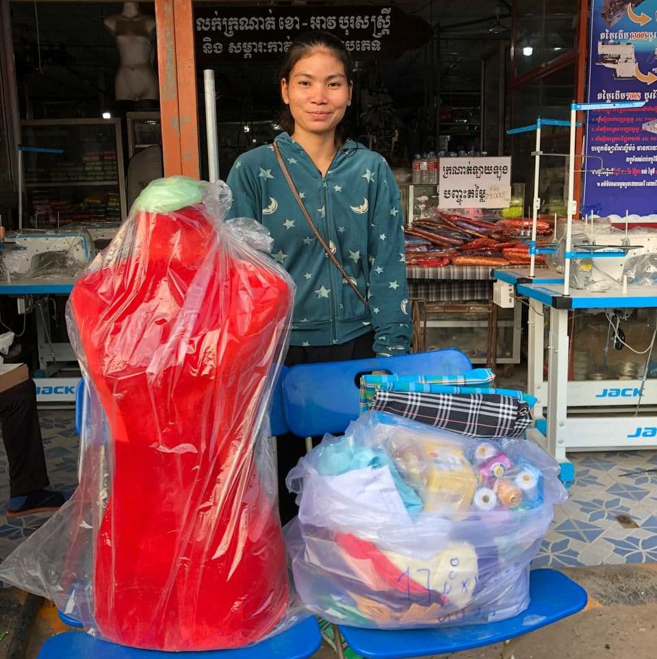 woman proudly standing behind sewing supplies and mannequin