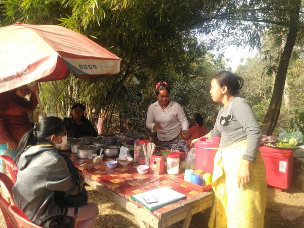 woman serving noodles to customers at outdoor stand