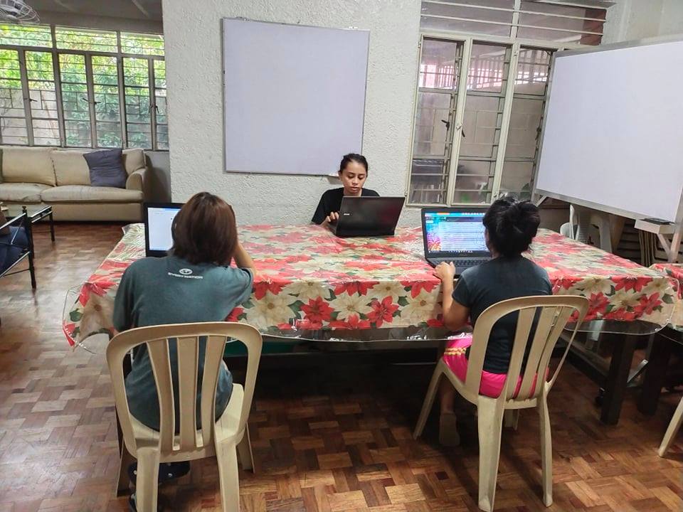 three students sitting on laptops at a big table