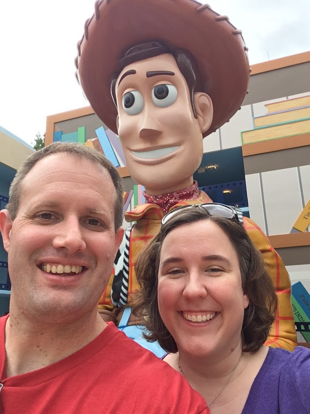 selfie of smiling man and woman in front of statue of cowboy