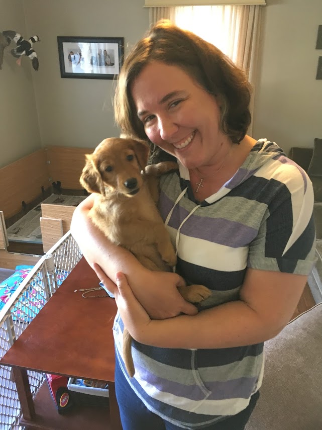 smiling woman holding golden puppy