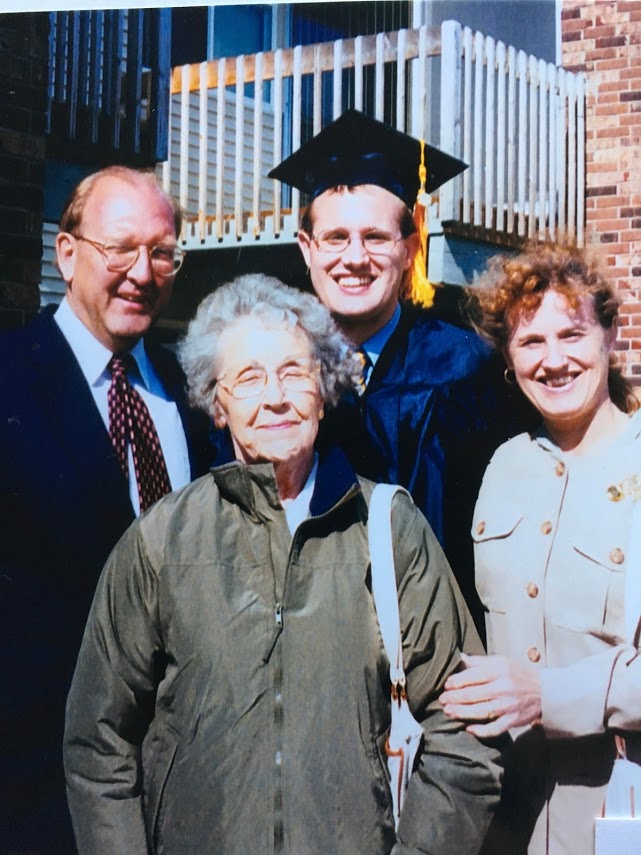 three people standing with man wearing graduation cap and gown