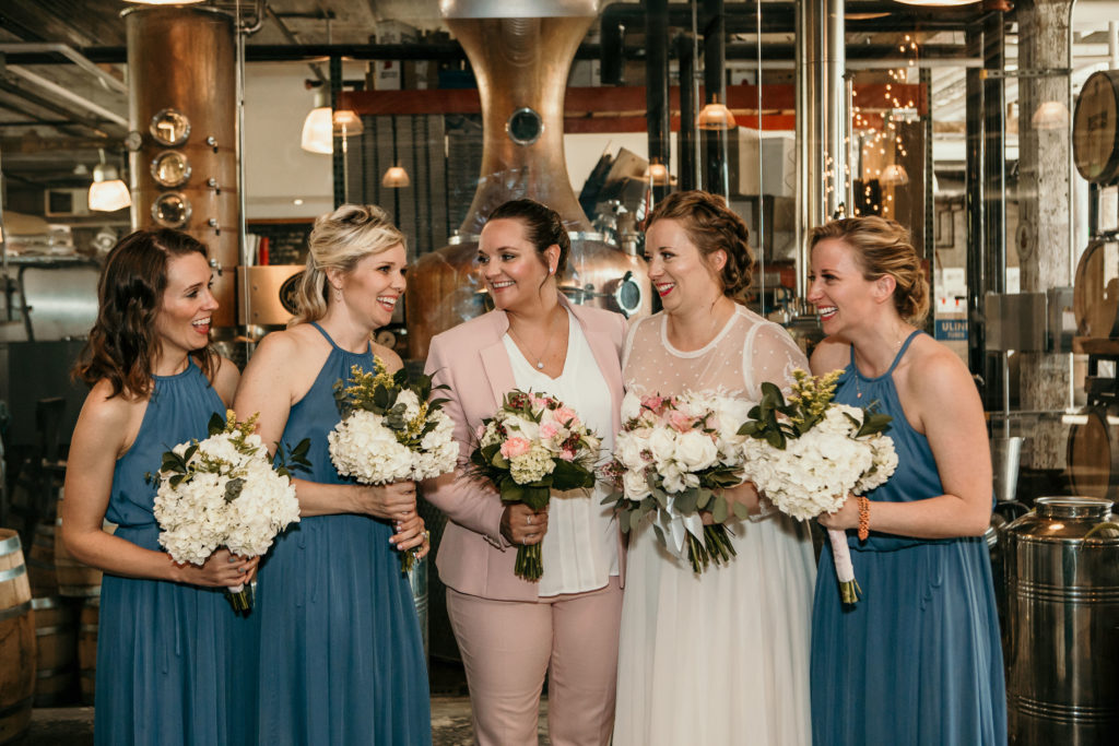three women in teal dresses one woman in wedding dress one woman in suit laughing together