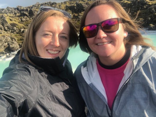 selfie of two women smiling in front of light blue lake