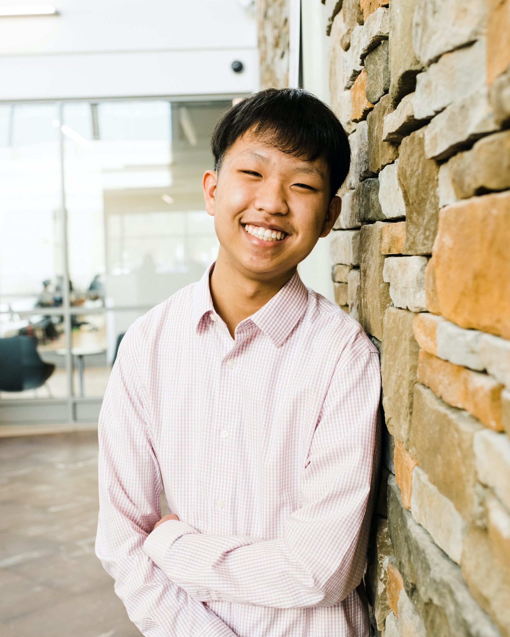 smiling man wearing button up shirt leaning against stone wall