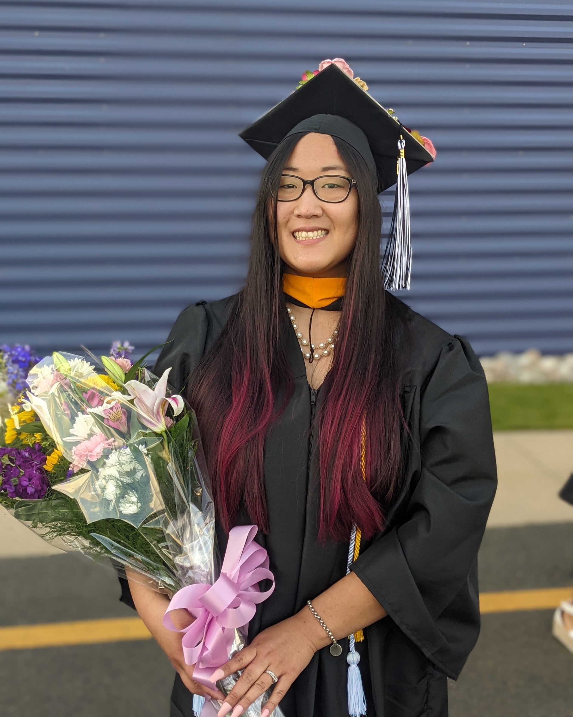 smiling girl wearing black graduation cap and gown holding bouquet of flowers