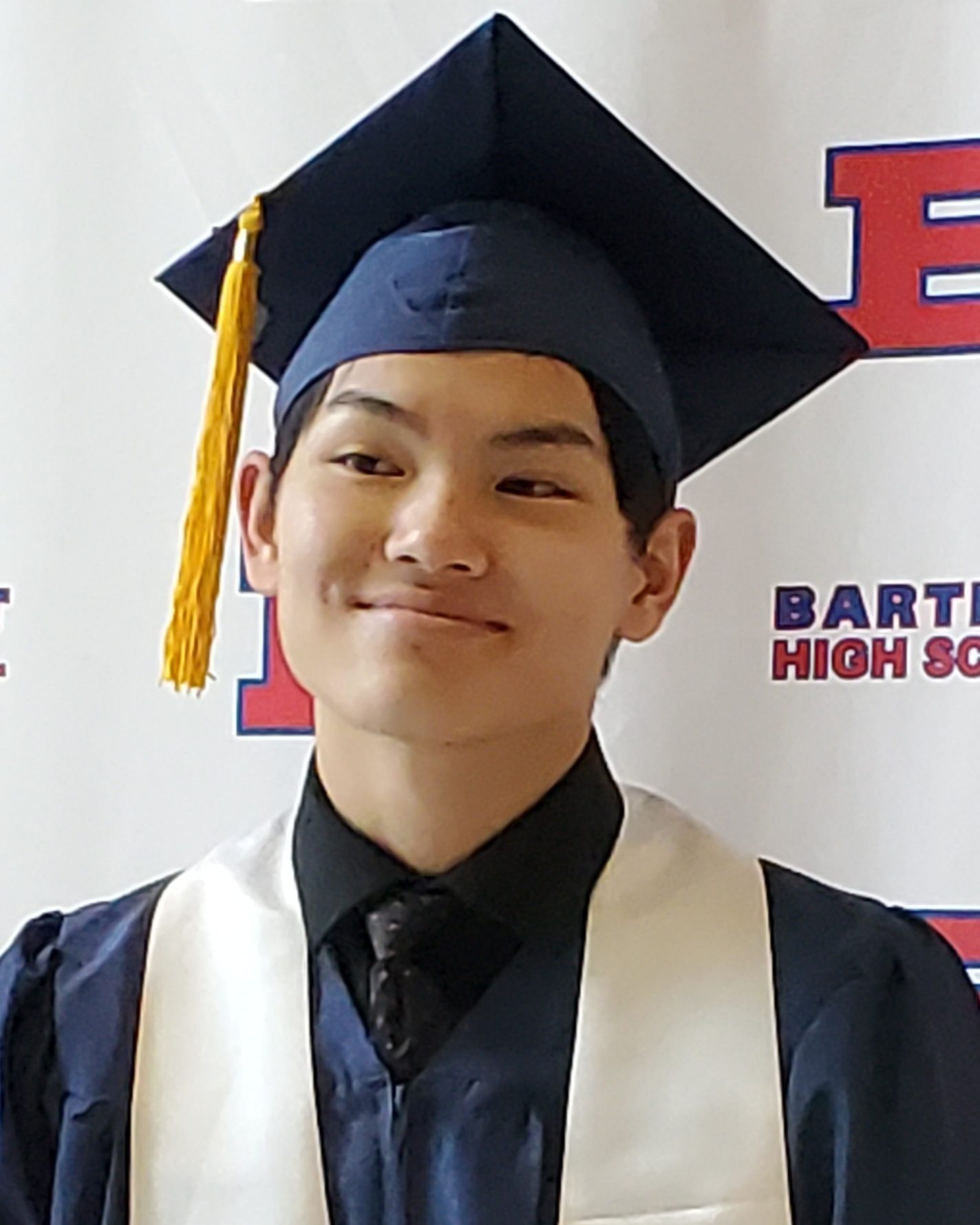 smiling man wering navy blue graduation cap and gown and white sash