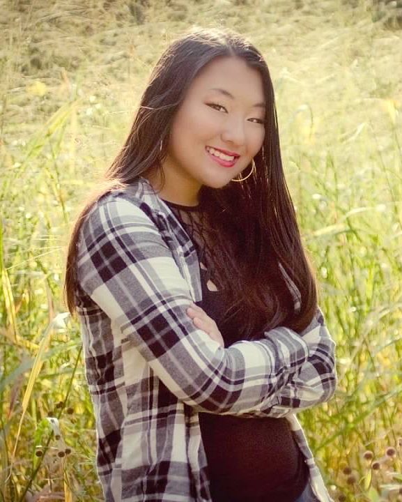 smiling girl with arms crossed standing in grassy field