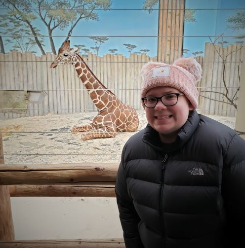smiling woman in pink beanie in front of giraffe