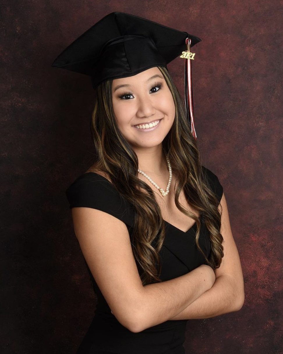 smiling girl with arms crossed wearing black graduation cap black off the shoulder shirt and pearl necklace