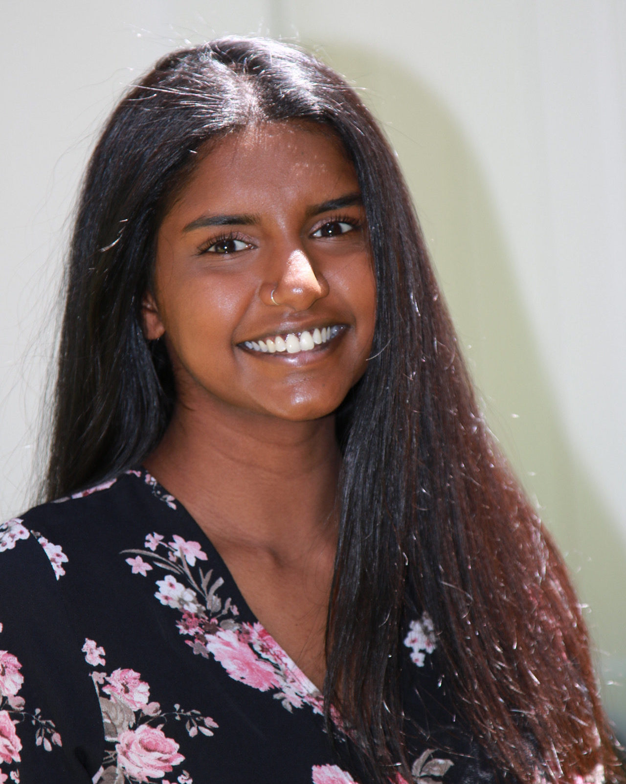 smiling girl with long brown hair wearing black and pink floral top