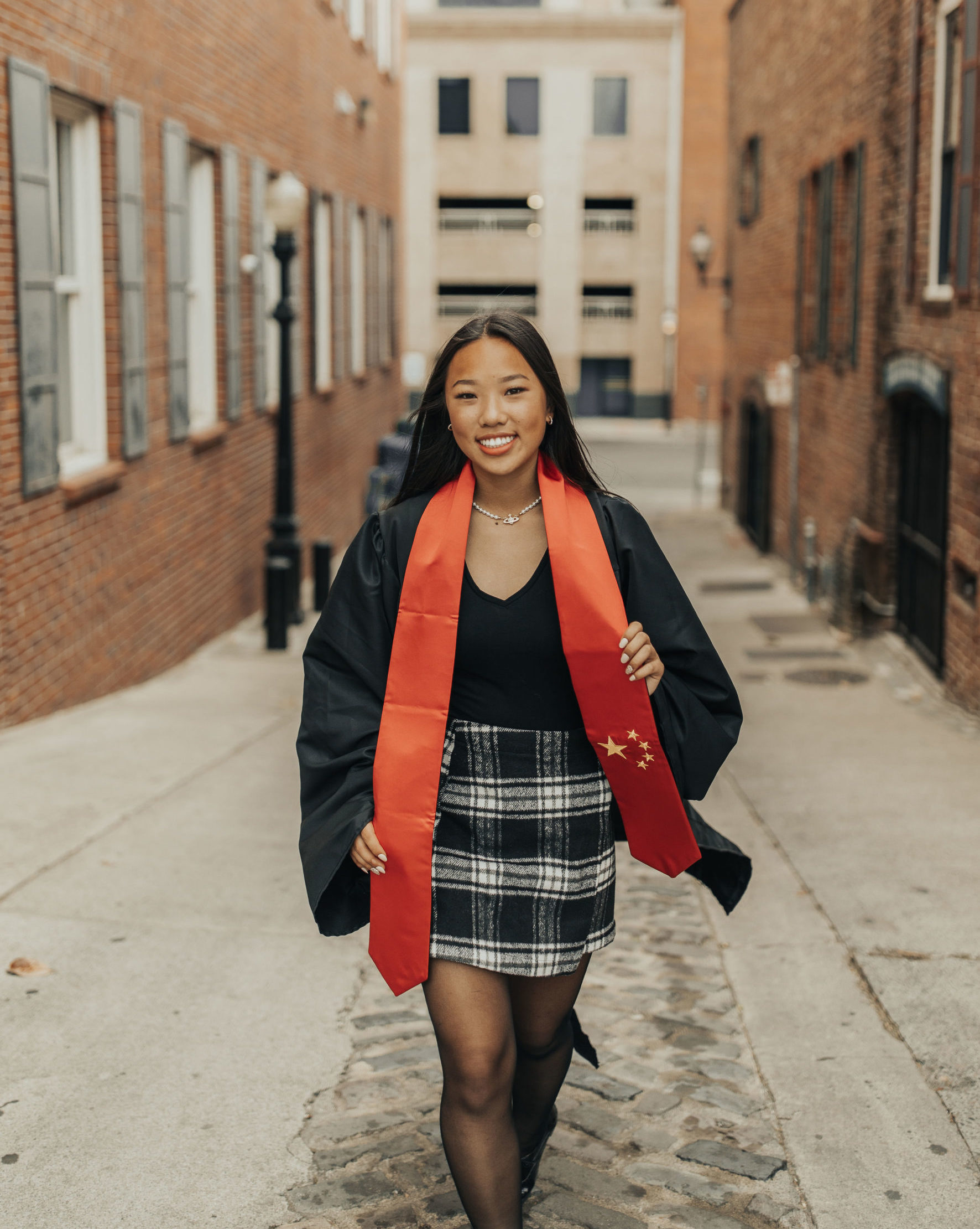smiling girl walking down alleyway wearing red sash printed like chinese flag