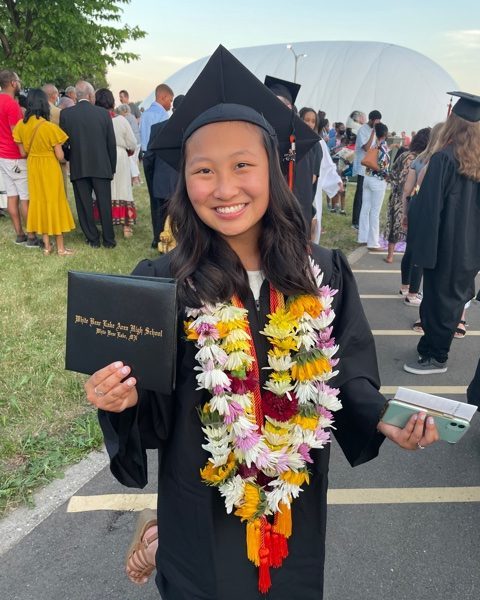 smiling girl wearing black graduation cap and gown lei necklaces and holding diploma cover