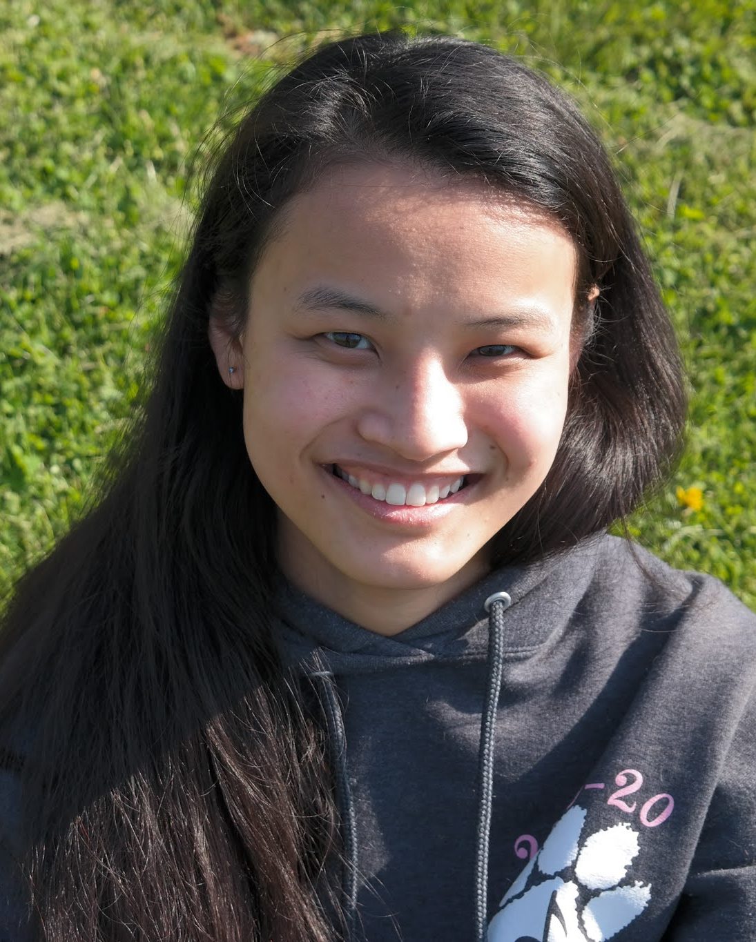 smiling girl sitting in field wearing grey sweatshirt
