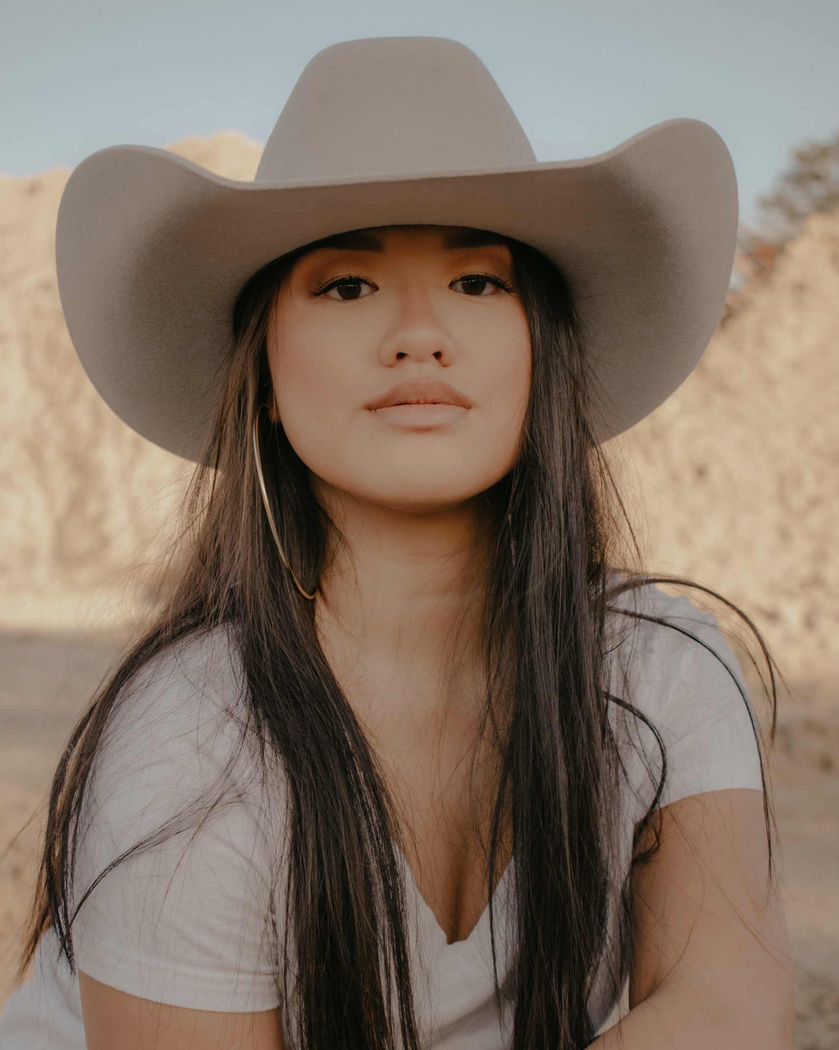 girl in front of desert background wearing white shirt and beige cowgirl hat