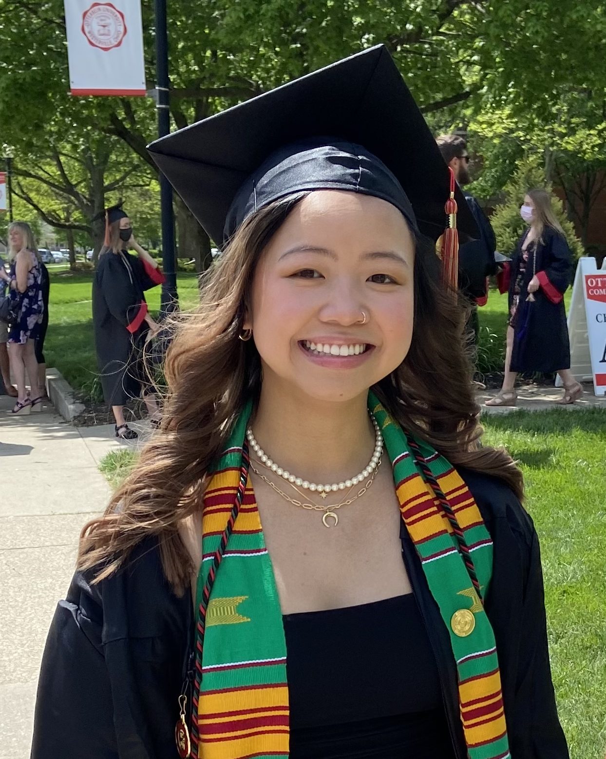 smiling girl wearing black graduation gown and cap and green orange and red sash