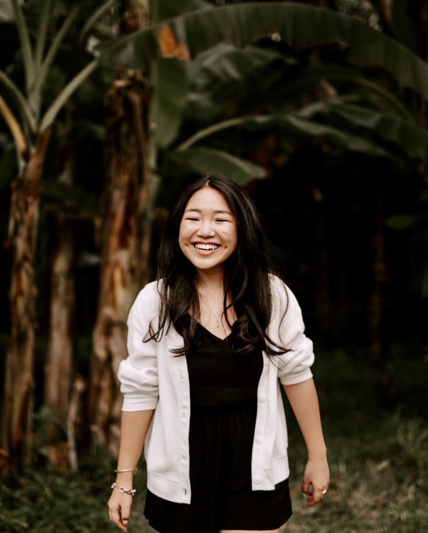 laughing girl in front of palm trees wearing white cardigan and black dress