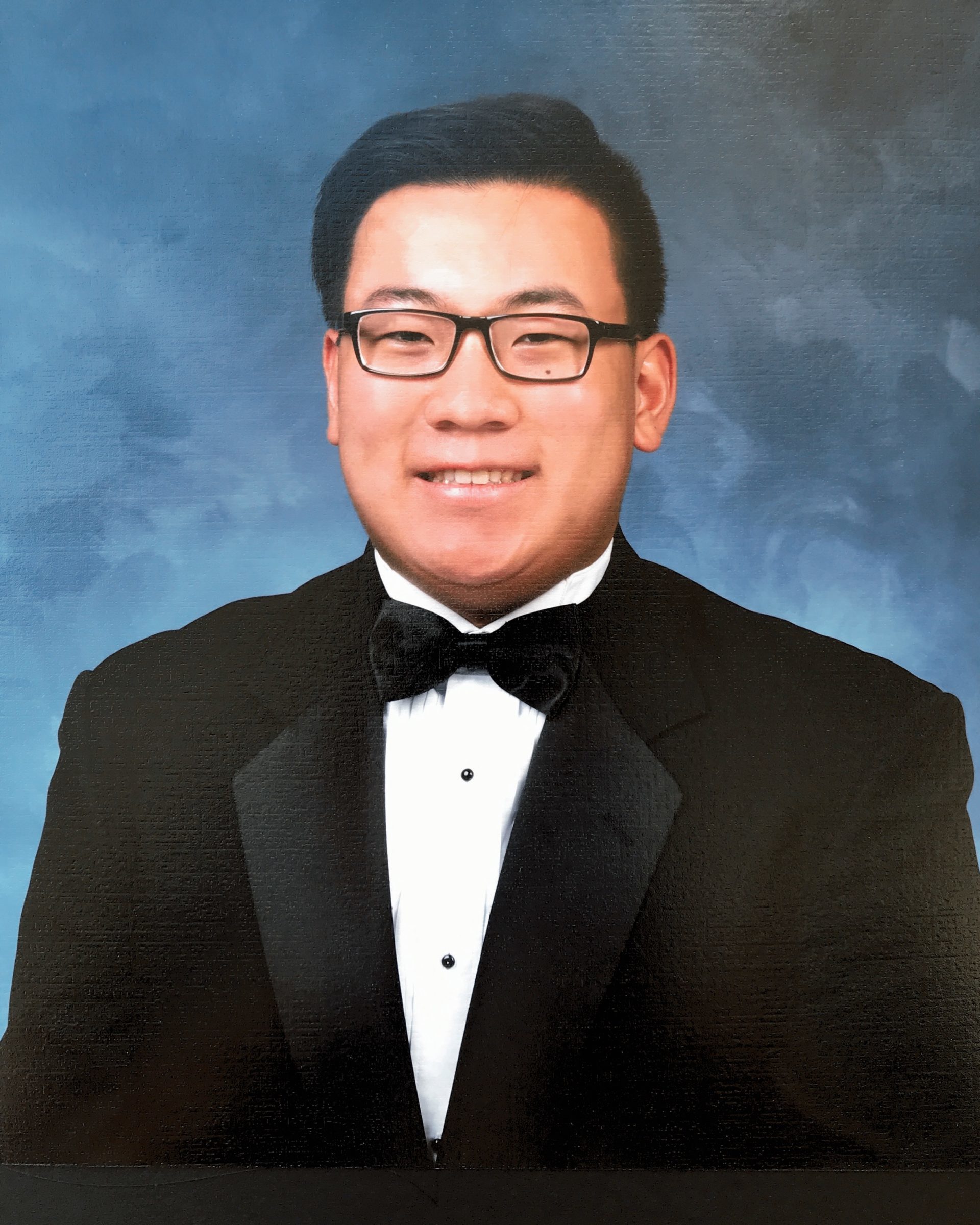 school photo of smiling man in black tuxedo and glasses