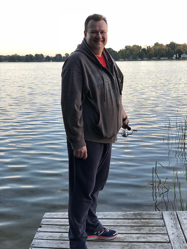 man standing on a pier in front of a clear lake