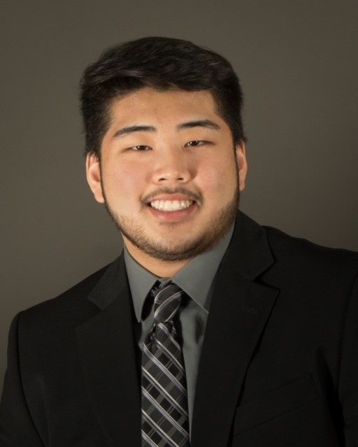 smiling man wearing black suit green shirt and black plaid tie