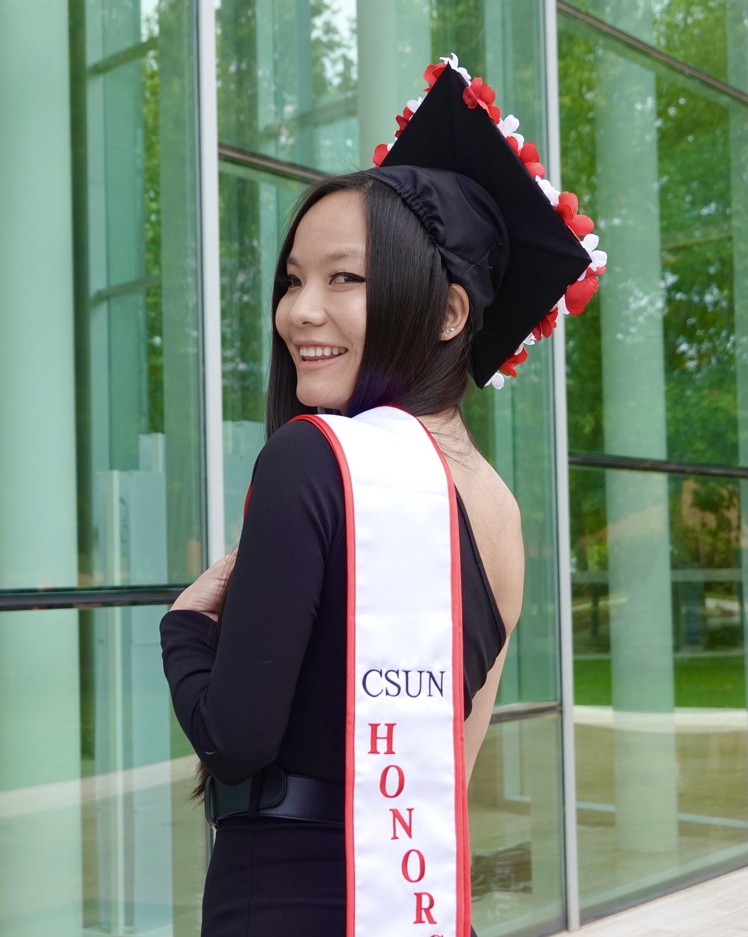 smiling girl wearing black dress graduation cap and white sash that says "csun honors"